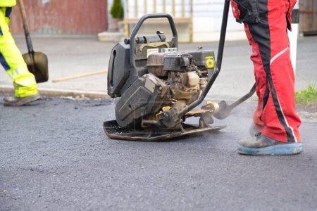 Foto de Trabajador de la construcción con placa de vibración durante el pavimento de asfalto - placa vibratoria, primer plano - Imagen libre de derechos