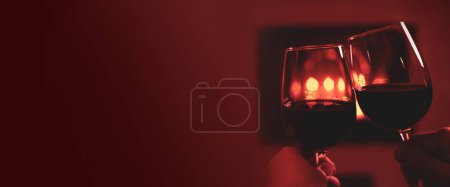 Photo for Couple making a toast with two glasses of red wine - burgundy banner. Fireplace as background - free copy (text) space. Christmas, romantic date or Valentine's Day mood. - Royalty Free Image