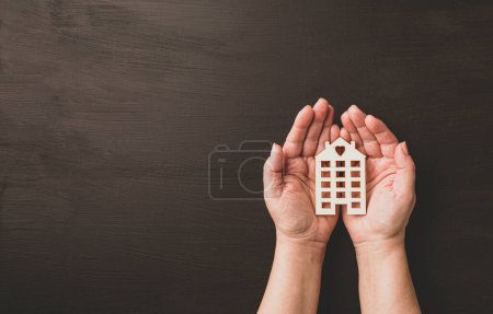 Téléchargez les photos : Hands holding wooden model of the house. Real estate, insurance and mortgage loans related concept. Black chalkboard background with free copy (text) space. - en image libre de droit