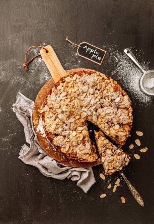 Foto de Homemade apple pie with flaked almonds crumble. Cake dessert captured from above (top view, flat lay) on a black chalkboard background. Free copy (text) space. - Imagen libre de derechos