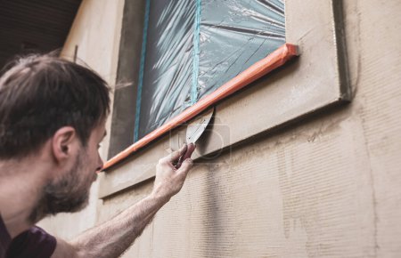Foto de Worker man (plasterer) plastering exterior walls of a house. Renovation of the building facade - construction industry. - Imagen libre de derechos