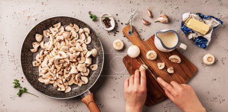 Téléchargez les photos : Cuisson - préparation de sauce aux champignons crémeuse sur une casserole. Les mains du chef coupent les ingrédients de la recette sur une planche en bois. Plan de travail de la cuisine capturé d'en haut (vue de dessus, plan plat). - en image libre de droit