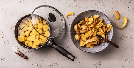 Foto de Cooking - preparing boiled potatoes. Pot and bowl with potato peels - kitchen worktop captured from above (top view, flat lay). - Imagen libre de derechos