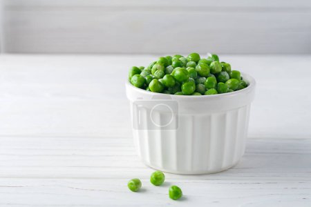 Photo for Freshly frozen green peas in a white bowl on a white wooden background - Royalty Free Image