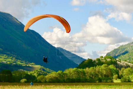 Paraglider tandem landing on the field between mountains in bright sunny evening in Accous, France. Conceptual for extreme sport and active lifestyle.