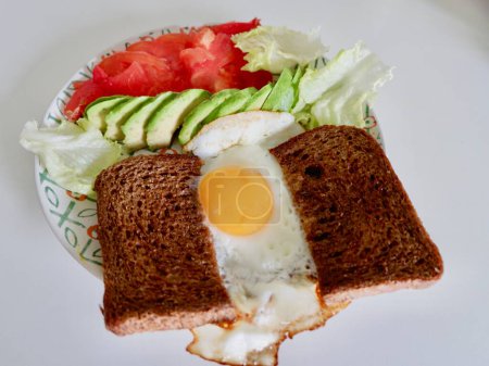Healthy brunch with fried egg, two pieces of wholegrain dark bread, slices of avocado and tomatoes.