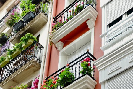 Foto de Mirada hacia arriba en fachadas coloridas con ventanas y pequeños balcones metálicos decorados con plantas de la casa en Bilbao, País Vasco, España. - Imagen libre de derechos