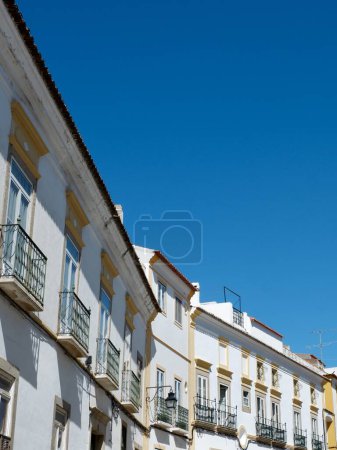 Line of old fashioned vintage facades of white colour against clear sky in Evora Portugal vertical backdrop.