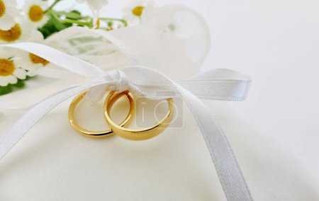 Gold wedding rings tied up with ribbon on white ring pillow and small flowers