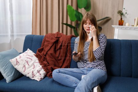 Foto de Llorando mujer limpiando lágrimas mientras viendo la televisión en casa - Imagen libre de derechos