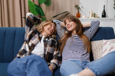 Photo for Lazy mother and daughter are lying on the sofa with their hands above their heads. Two women of different ages laughing are relaxing on the couch - Royalty Free Image