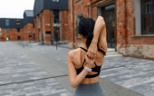 Athletic woman exercising yoga pose and clasping hands behind her back on lock, rear view against brick building Poster #620436020