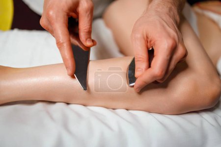 Photo for Masseur using IASTM instrument for soft tissue treatment on the leg of a female patient - Royalty Free Image