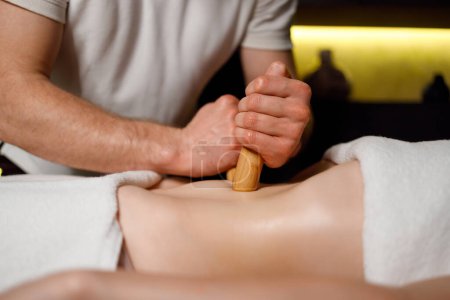 Téléchargez les photos : Close up view hands of a strong masseur massage the female abdomen with bamboo sticks - en image libre de droit