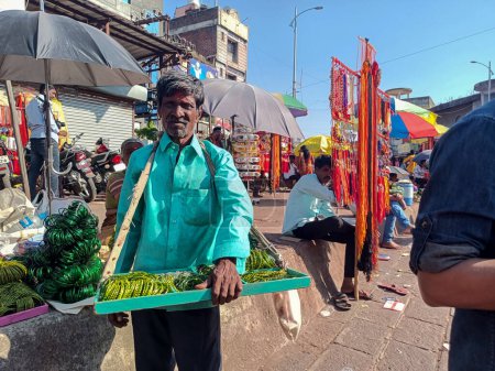 Photo for Tulajapur,India- October 28th 2022; Stock photo of 60 to 70 aged Indian man wearing blue color shirt and black color pant selling green color glass bangles in the market area under bright sunny day. - Royalty Free Image