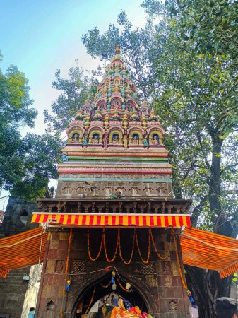 Photo for Inside view of popular holy temple In Maharashtra state tuljabhavani mata Mandir tuljapur. dravidian style temple tower, sculpture of god and goddess on the spire, green trees, sky on background. - Royalty Free Image