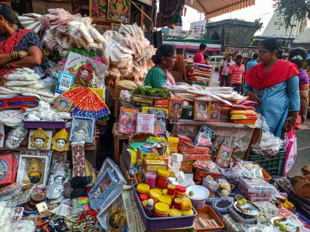 Téléchargez les photos : Kolhapur, Maharashtra, Inde- 6 novembre 2022 ; photo de stock de livres, déesse visage mural, chiffons, guirlande de coton articles utilisés pour adorer dieu, gardé dans une boutique à vendre les gens qui achètent des articles auprès du vendeur. - en image libre de droit