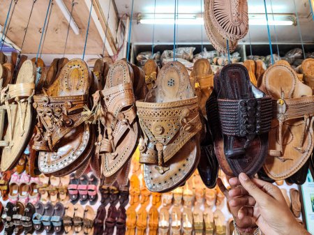 Photo for Stock photo of popular and traditional kolhapuri chappal hanging in the display for sale in the local shop.It is handmade leather chappal with unique design and color at Kolhapur, Maharashtra, India. - Royalty Free Image