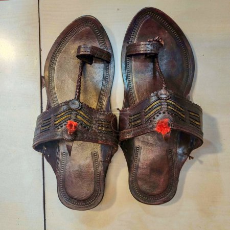 Photo for Stock photo of popular and traditional dark brown color handmade kolhapuri chappal for men, Picture captured under bright light at Kolhapur, Maharashtra, India. white color marble floor on background - Royalty Free Image