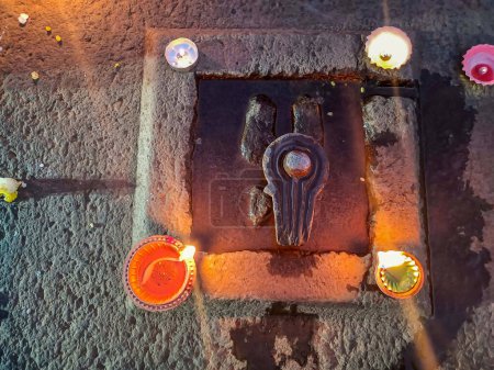 Foto de Foto de stock muestra un antiguo Shivling tallado en piedra con pequeñas lámparas de aceite decoradas a su alrededor, capturado temprano en la mañana en Kolhapur, Maharashtra, India. - Imagen libre de derechos