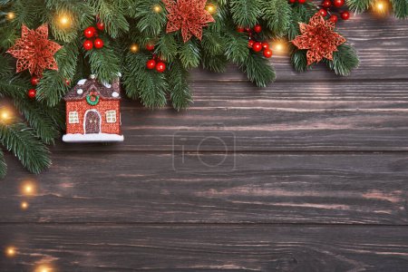 Photo for Christmas or New Year background with fir branches and decorative house on a wooden backdrop. Happy Holidays concept in minimalistic style. Flat lay, Copy space, Mock up - Royalty Free Image
