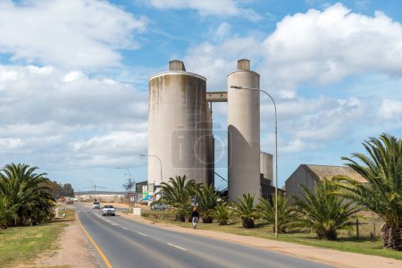 Photo for Bredasdorp, South Africa - Sep 23, 2022: A street scene, with grain silos, palm trees and vehicles, in Bredasdorp in the Western Cape Province - Royalty Free Image