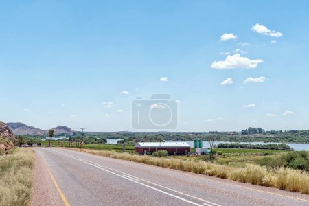 Photo for Upington, South Africa - Feb 24, 2023: A road scene, with buildings and the flooded Orange River, on road N10 near Leerkrans in the Northern Cape Province - Royalty Free Image