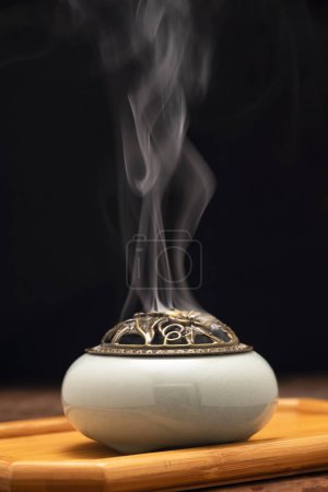 Räucherstäbchen brennen in einem Räucherofen auf dem Tisch, mit dunklem Hintergrund. Religionskonzept.