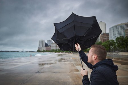 Mann mit kaputtem Regenschirm bei starkem Wind an trübem Regentag in der Stadt