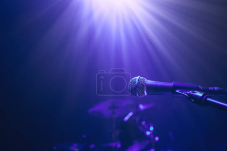 Foto de Enfoque selectivo en micrófono lluminado contra kit de batería en el escenario en luz azul - Imagen libre de derechos