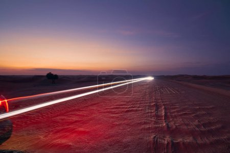 Téléchargez les photos : Sentiers lumineux de voiture sur la route déserte dans les dunes de sable milieu. Abu Dhabi, Émirats arabes unis - en image libre de droit
