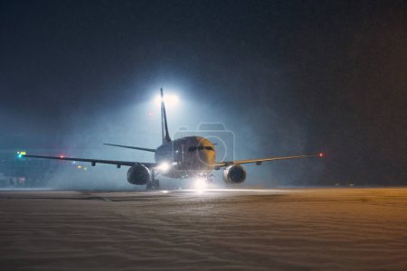 Photo for Winter night at airport. Airplane taxiing to runway for take off during heavy snowfall - Royalty Free Image