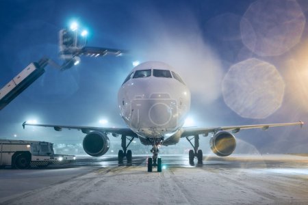 Téléchargez les photos : Dégivrage de l'avion avant le vol. Nuit d'hiver à l'aéroport pendant les chutes de neige - en image libre de droit