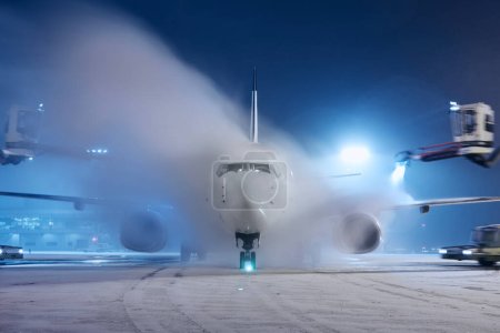 Deicing of airplane before flight. Winter night at airport during snowfall.