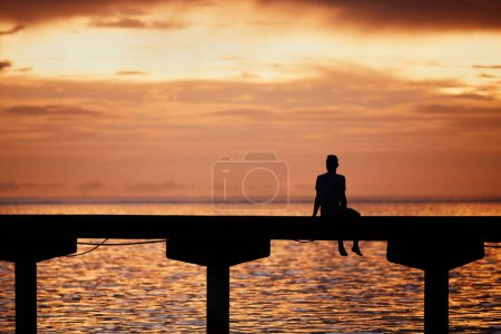 Foto de Hombre pensando en el borde del muelle y mirando al océano al atardecer dorado. - Imagen libre de derechos