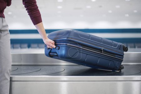 Photo for Traveling by airplane. Passenger pick up his blue suitcase in baggage claim in airport terminal. - Royalty Free Image