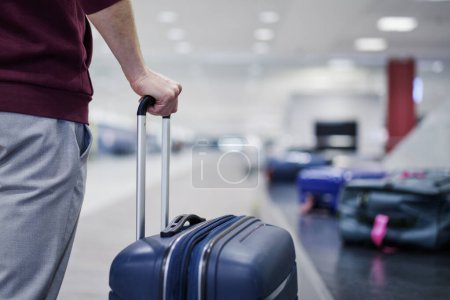Téléchargez les photos : Traveling by airplane. Passenger holding his suitcase in baggage claim in airport terminal - en image libre de droit