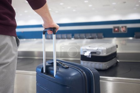 Foto de Traveling by airplane. Passenger holding his suitcase in baggage claim in airport terminal. - Imagen libre de derechos