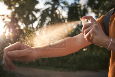 Photo for Man is applying insect repellent on his hand against palm trees. Prevention against mosquito bite in tropical destination. - Royalty Free Image