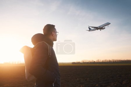 Téléchargez les photos : Homme avec sac à dos regardant vers l'atterrissage de l'avion à l'aéroport pendant le beau coucher de soleil. - en image libre de droit