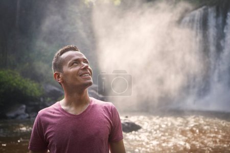 Foto de Retrato de viajero contra cascada alta. Hombre feliz en la naturaleza tropical en Camboya - Imagen libre de derechos