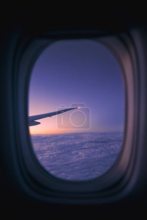 Téléchargez les photos : Vue de la fenêtre de l'avion pendant le vol au-dessus des nuages à l'aube. Concentration sélective sur l'aile de l'aéronef - en image libre de droit