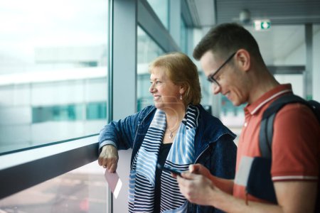 Téléchargez les photos : Passagers en attente à l'aéroport. Heureuse femme âgée avec son fils adulte avant d'embarquer dans l'avion - en image libre de droit