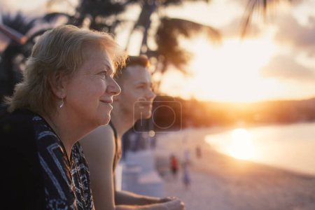 Téléchargez les photos : Portrait de femme âgée avec son fils adulte regardant ensemble la plage de sable et la mer au beau coucher de soleil. - en image libre de droit