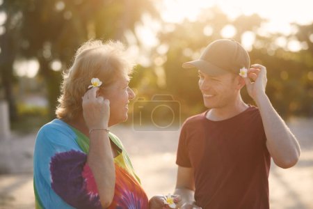 Téléchargez les photos : Heureuse femme âgée avec son fils adulte ensemble sur la plage au beau coucher de soleil. Touristes en destination tropicale - en image libre de droit