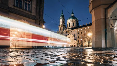 Téléchargez les photos : Sentier lumineux de tramway passant entre les bâtiments historiques la nuit. Galets humides dans la petite ville de Prague, République tchèque - en image libre de droit