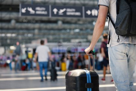 Anreise mit dem Flugzeug. Selektiver Fokus auf die Hand des Kofferhalters. Reisender läuft mit Gepäck durch Flughafenterminal zum Check-in.
