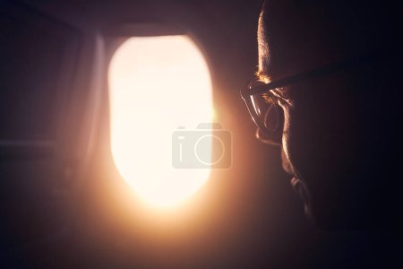 Téléchargez les photos : Portrait d'homme en avion. Concentration sélective sur le passager en regardant par la fenêtre pendant le vol au coucher du soleil - en image libre de droit