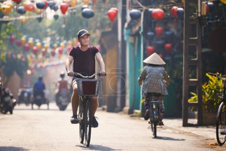 Photo for Tourist riding bicycle in old town. Street of ancient city decorated with traditional lanterns, Hoi An, Vietnam. - Royalty Free Image
