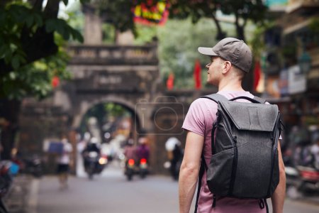Reisende, die auf einer belebten asiatischen Straße spazieren gehen. Rückansicht eines Mannes mit Rucksack in der Altstadt von Hanoi, Vietnam.